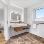 Badezimmer mit Waschbecken, Spiegel und Fenster. Durchgang zu Schlafzimmer mit Bett.