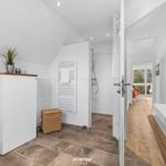 Badezimmer mit Dusche, Badewanne und Toilette. Holzboden und weiße Fliesen.