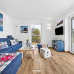 Wohnzimmer mit blauem Sofa, Holzboden und großen Fenstern.