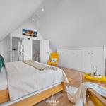 Schlafzimmer mit Dachschrägen, Bett, gelben Sesseln und weißen Schränken.