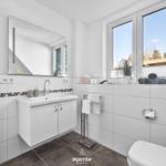 Badezimmer mit Waschbecken, Spiegel, Fenster und Toilette.