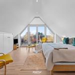 Schlafzimmer mit großem Bett, gelben Sesseln und großem Fenster zur Terrasse.