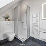 Badezimmer mit Dusche, Waschbecken und Toilette unter Dachschräge