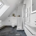 Badezimmer mit Dusche, Waschbecken und Toilette unter Dachschrägen.