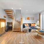 Wohnraum mit Holzdielen, Sofa, Treppe und Balkontür.