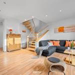 Wohnzimmer mit Sofa, Tisch und Treppe. Holzboden und Wandbild mit Strandmotiv.