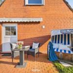 Terrasse mit Strandkorb, Tisch und Stühlen vor rotem Backsteinhaus.