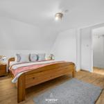 Schlafzimmer mit Holzbett, Nachttisch und Teppich. Tür führt in angrenzenden Raum.