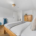 Schlafzimmer mit Holzbett, Kleiderschrank und Sessel.