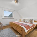 Schlafzimmer mit Holzbett, Nachttisch und Sessel unter Dachschrägen.