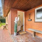 Eingangsbereich mit Holzveranda, Steinbank und Pflanze. Tür mit Glas und Briefkasten an der Wand.