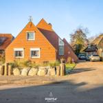 Rotes Backsteingebäude mit Dachgaube und Windschutz. Vorhof mit Stein- und Holzumrandung.