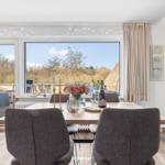 Esszimmer mit Tisch, Stühlen und Aussicht auf Balkon und Wald.