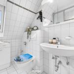 Badezimmer mit Toilette, Waschbecken und Fenster. Weiße Fliesen und Spiegelschrank.