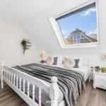 Schlafzimmer mit Dachfenster, weißem Bett und zwei Sitzbänken mit rotem Sitzkissen.