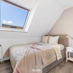 Schlafzimmer mit Dachschrägen, Bett, Nachttisch und Fenster mit Blick auf Dach.