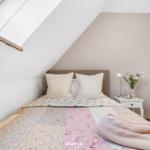 Schlafzimmer mit Dachschrägen, Bett mit Blumenbezug und Nachttisch mit Lampe.