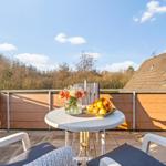 Terrasse mit Tisch, Stühlen und Obstschale. Blick auf Wald und Häuser.