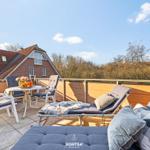 Terrasse mit Liegestühlen, Tisch und Sicht auf Haus und Wald.