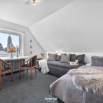 Schlafzimmer mit Dachschrägen, Bett, Sofa und Fenster mit Blick auf Kirche.