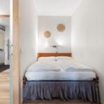 Schlafzimmer mit Doppelbett und Küchenbereich im Hintergrund.