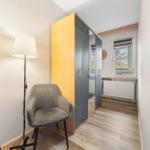 Schlafzimmer mit Kleiderschrank, Stuhl und Stehlampe. Fenster mit Blick nach draußen.