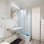 Badezimmer mit Dusche, Waschbecken und Toilette. Weiße Fliesen und Schränke.