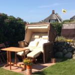 Außenbereich mit Liegestuhl, Tisch und Blumen. Hintergrund: Steinmauer und traditionelle Häuser.