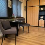 Zimmer mit Tisch, zwei Stühlen, Bücherregal und Fenster mit Jalousien.