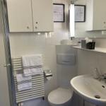 Badezimmer mit Dusche, Waschbecken und Toilette. Weiße Fliesen und Handtücher.