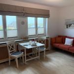 Wohnzimmer mit Sofa, Esstisch und Fensterblick auf Dächer