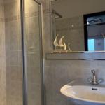 Badezimmer mit Dusche, Waschbecken und Spiegel. Dekorative Segelboote auf der Ablage.