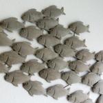 Wanddekoration mit Fischfiguren aus Metall an einer weißen Wand.