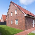Rotes Ziegelhaus mit Garten und Terrasse unter blauem Himmel.