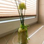 Glasvase mit grünen Blumen auf Fensterbank