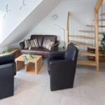 Wohnzimmer mit Sofa, zwei Sesseln, Tisch und Holztreppe
