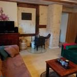 Wohnzimmer mit grünem Sofa, Holztisch und Kaminofen. Wandbild und Fenster sichtbar.