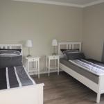 Zwei Einzelbetten mit Nachttischen und Lampen. Fenster mit Vorhang.