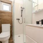 Bathroom with shower, sink and toilet. Wood wall and window.