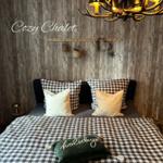 Schlafzimmer mit Holzwand, Bett mit kariertem Bettzeug und Hirschgeweih-Leuchter.