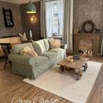 Ein Wohnzimmer mit Sofa, Kamin und Holzboden. An der Wand hängt eine Lampe.