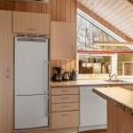 Küche mit Kühlschrank, Spüle und Fenster. Holzwände und Arbeitsplatte.