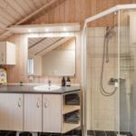 Badezimmer mit Dusche, Waschbecken und Spiegel unter Holzdecke.