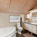 Badezimmer mit Badewanne, Toilette und Waschbecken unter Holzdecke.