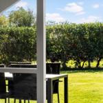 Durch die offene Tür blickt man auf einen grünen Garten mit Bäumen und einem Tisch mit Stühlen.