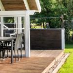 Terrasse mit Tisch und Stühlen, Holzdecke und grüner Rasenfläche.