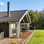 Haus mit Holzterrasse, Grill und Sitzgelegenheiten im Garten.