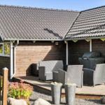 Holzhaus mit Terrasse, Gartenmöbeln und Grill. Umgeben von Pflanzen und Steinen.