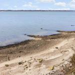 Strand mit Steinen und Sand, Blick auf ruhiges Wasser und Horizont.