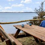 Holztisch und Bänke am Wasser mit Decken und Tassen.